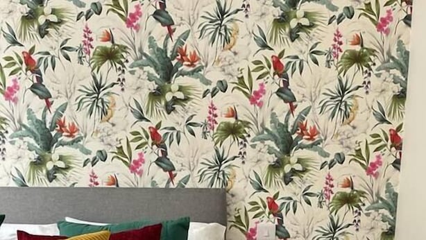 A bed with multiple pillows, a bedside table with a lamp, and a floral wallpaper pattern. - NEW & Vibrant 1-Bed in Town Centre w/ Free Parking (Bournemouth)