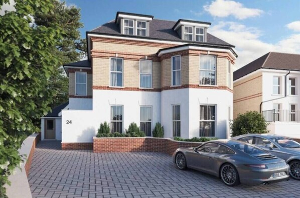 A modern two-story house with a brick facade, numbered 24, featuring a driveway and two parked cars.