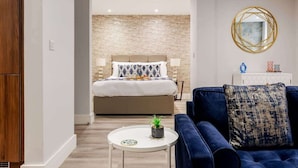 A modern hotel room with a large bed, a blue sofa, a small round table with a plant, and a decorative mirror on the wall. - Delightful 1-bed Studio w/ Free Parking & WiFi (Bournemouth)