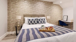 A modern bedroom with a brick-patterned wall, a bed with striped bedding, and a tray of breakfast on the bed. - Delightful 1-bed Studio w/ Free Parking & WiFi (Bournemouth)