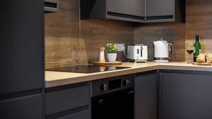 A modern kitchen with dark cabinetry, a wooden countertop, a coffee maker, a toaster, a wine glass, and a bottle of wine. - Wholesome Family 3-Bed, 2-Bath Apt; Free Gym & PKG (Bournemouth)
