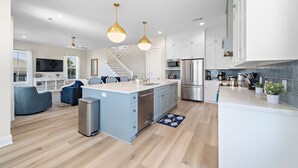 Een moderne keuken met een centraal kookeiland, roestvrijstalen apparatuur en hanglampen.