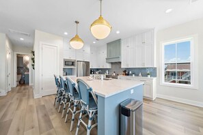 Una cocina moderna con armarios blancos, una isla central con taburetes de bar, electrodomésticos de acero inoxidable e iluminación colgante.