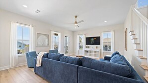 Een ruime woonkamer met een grote blauwe hoekbank, een plafondventilator en een flatscreen televisie op een witte entertainmentkast.