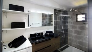 Un baño moderno con un lavamanos negro, un espejo, una ducha y un perchero para toallas.
