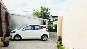Un coche blanco estacionado en un camino de hormigón con plantas en macetas y un edificio al fondo.