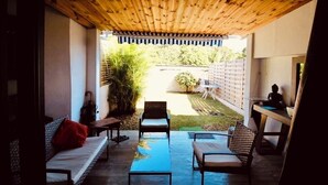 Un patio exterior con techo de madera, un sofá, dos sillas y una mesita.