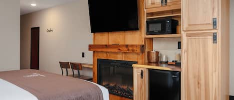 A hotel room with a bed, a fireplace, a television, a microwave, and a refrigerator.