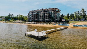 A multi-story hotel with balconies, a beach area with sun loungers, and a dock extending into the water. - Tamarack Lodge of Traverse City (Traverse City)