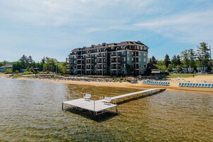 Un hotel de varios pisos con balcones, una zona de playa con tumbonas y un muelle que se adentra en el agua.