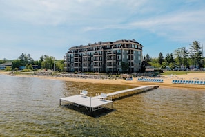 Un hôtel à plusieurs étages doté de balcons, une plage avec des chaises longues et une jetée s’avançant dans l’eau.