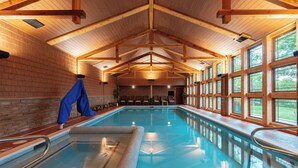 An indoor swimming pool with wooden beams, a tiled floor, and large windows. - Tamarack Lodge of Traverse City (Traverse City)