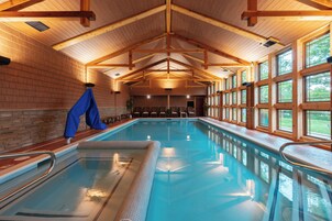 Una piscina interior con vigas de madera, suelo de baldosas y ventanas amplias.