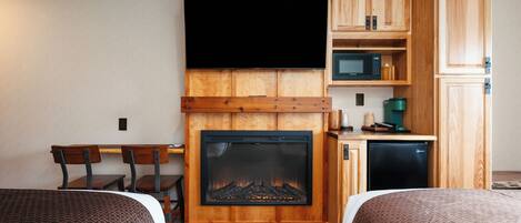 A hotel room with a fireplace, wooden cabinets, a television, a microwave, and a small refrigerator.