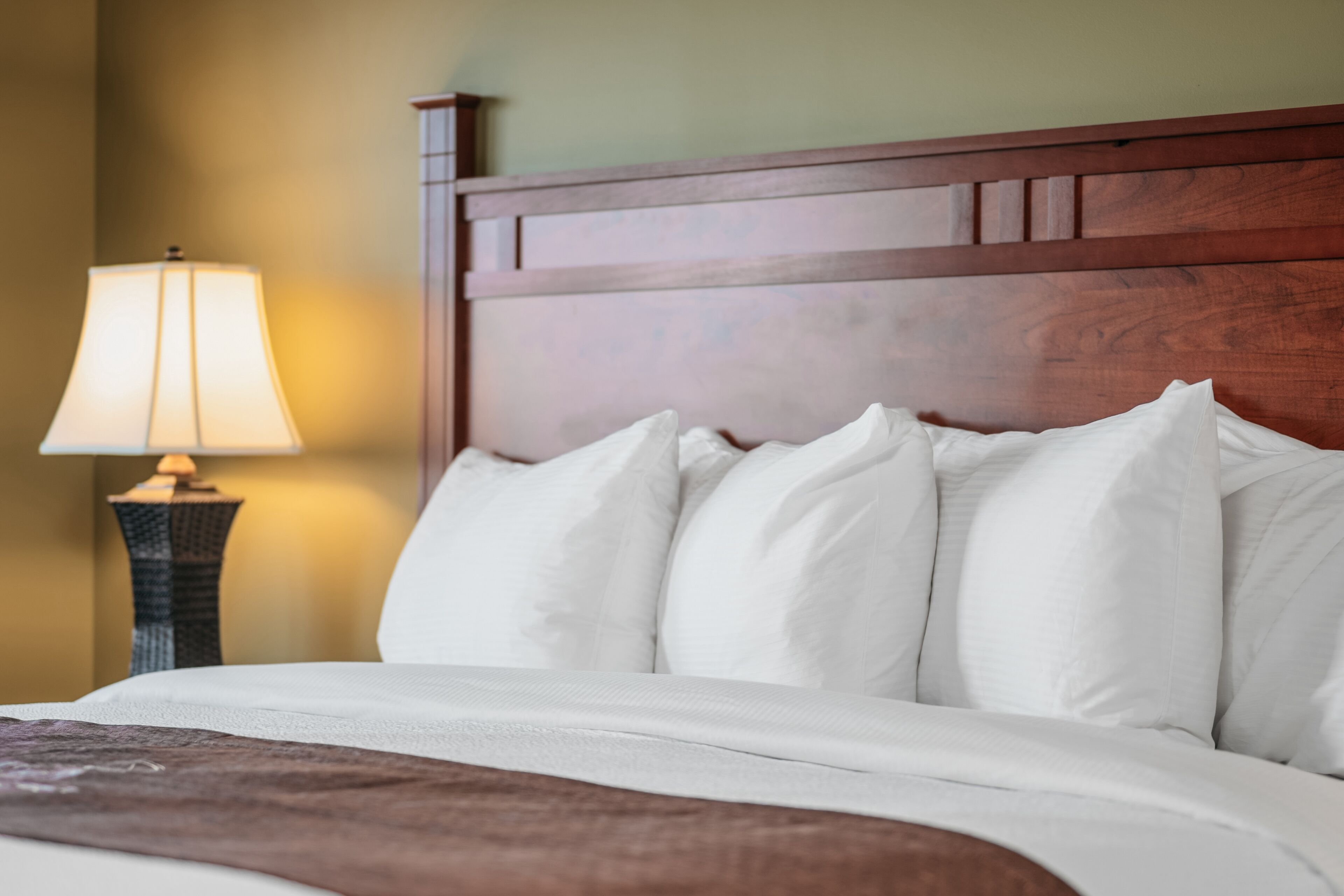 A neatly made bed with white linens and a wooden headboard.