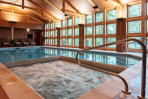 An indoor swimming pool with a hot tub, surrounded by large windows and wooden beams. - Tamarack Lodge of Traverse City (Traverse City)