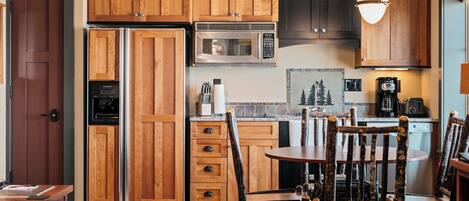 Una cocina con armarios de madera, un refrigerador de acero inoxidable, un microondas y una zona de comedor con una mesa y sillas.