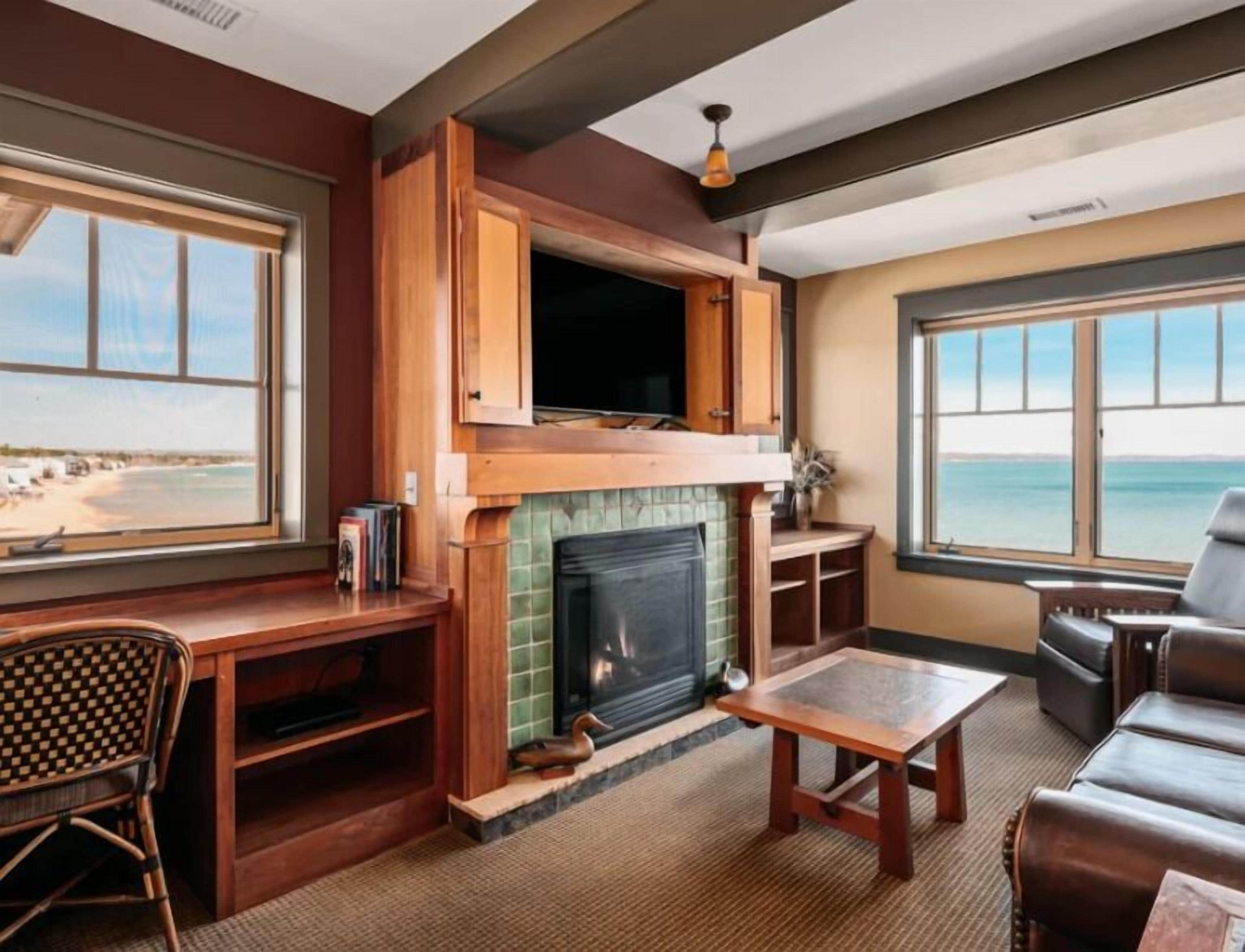 A living room with a fireplace, wooden furniture, and a view of the beach.