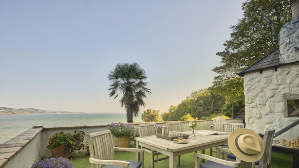A wooden deck with a table and chairs, overlooking a body of water. - 3 Bed - Smugglers Cottage (Torquay)