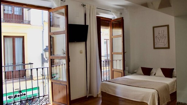 Une chambre avec un lit, une télévision et un balcon donnant sur la rue.