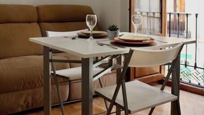 Un coin repas comprenant une table et des chaises, un canapé et une fenêtre donnant sur des immeubles.