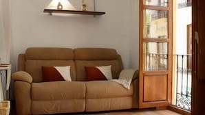Une pièce avec un canapé marron, un lit, une porte en bois et une petite étagère sur laquelle se trouve une lampe.