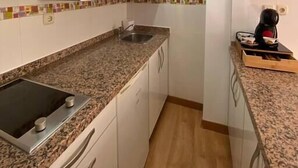 Une cuisine avec des meubles blancs, un plan de travail en granit, un évier en acier inoxydable et une cuisinière noire.