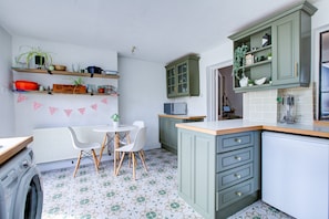 A kitchen with green cabinets, a white countertop, and a dining area with a table and chairs.