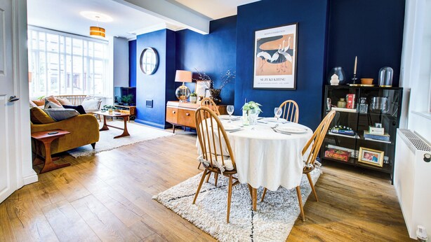 A dining area with a round table, chairs, and a blue accent wall. - Cosy house on the seafront - Pass the Keys (Southend-on-Sea)