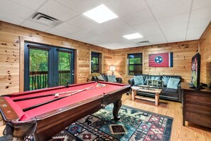 Una mesa de billar en una sala con paredes de madera, un sofá y una bandera.