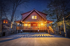 A wooden cabin with a porch, a staircase, and a clear night sky.