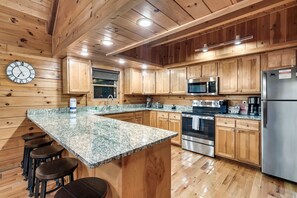 A kitchen with wooden cabinets, granite countertops, stainless steel appliances, and a clock on the wall. - 3 Min to Parkway | Private Resort Pool | Top 5%! (Pigeon Forge)