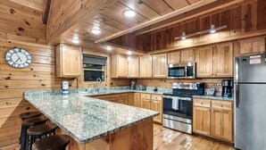 Una cocina con armarios de madera, encimeras de granito, electrodomésticos de acero inoxidable y un reloj en la pared.