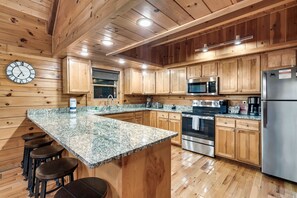 A kitchen with wooden cabinets, granite countertops, stainless steel appliances, and a clock on the wall.