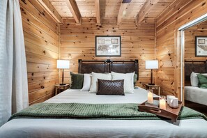 A wooden-paneled room with a bed, two bedside tables, a nightstand, a framed map on the wall, and a mirror.