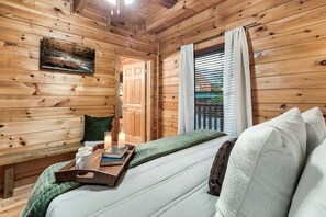 A wooden cabin room with a bed, a bedside table with candles, a tray with cups, and a painting on the wall. - 3 Min to Parkway | Private Resort Pool | Top 5%! (Pigeon Forge)