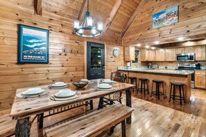 A wooden interior with a dining table set for four, a kitchen with modern appliances, and a sign indicating a Tennessee location. - 3 Min to Parkway | Private Resort Pool | Top 5%! (Pigeon Forge)