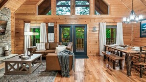 Una cabaña de madera espaciosa con un dormitorio en el altillo, una zona de estar acogedora con chimenea y un comedor.