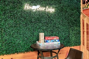 A table with board games and a neon sign reading "Honey Bear Lodge" against a green wall.