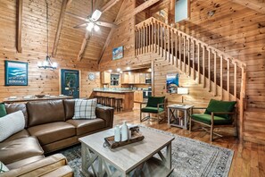 Interior de una cabaña de madera con sala de estar, cocina y una escalera.
