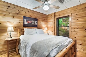 Un dormitorio con paneles de madera, una cama, mesitas de noche, lámparas y un ventilador de techo.