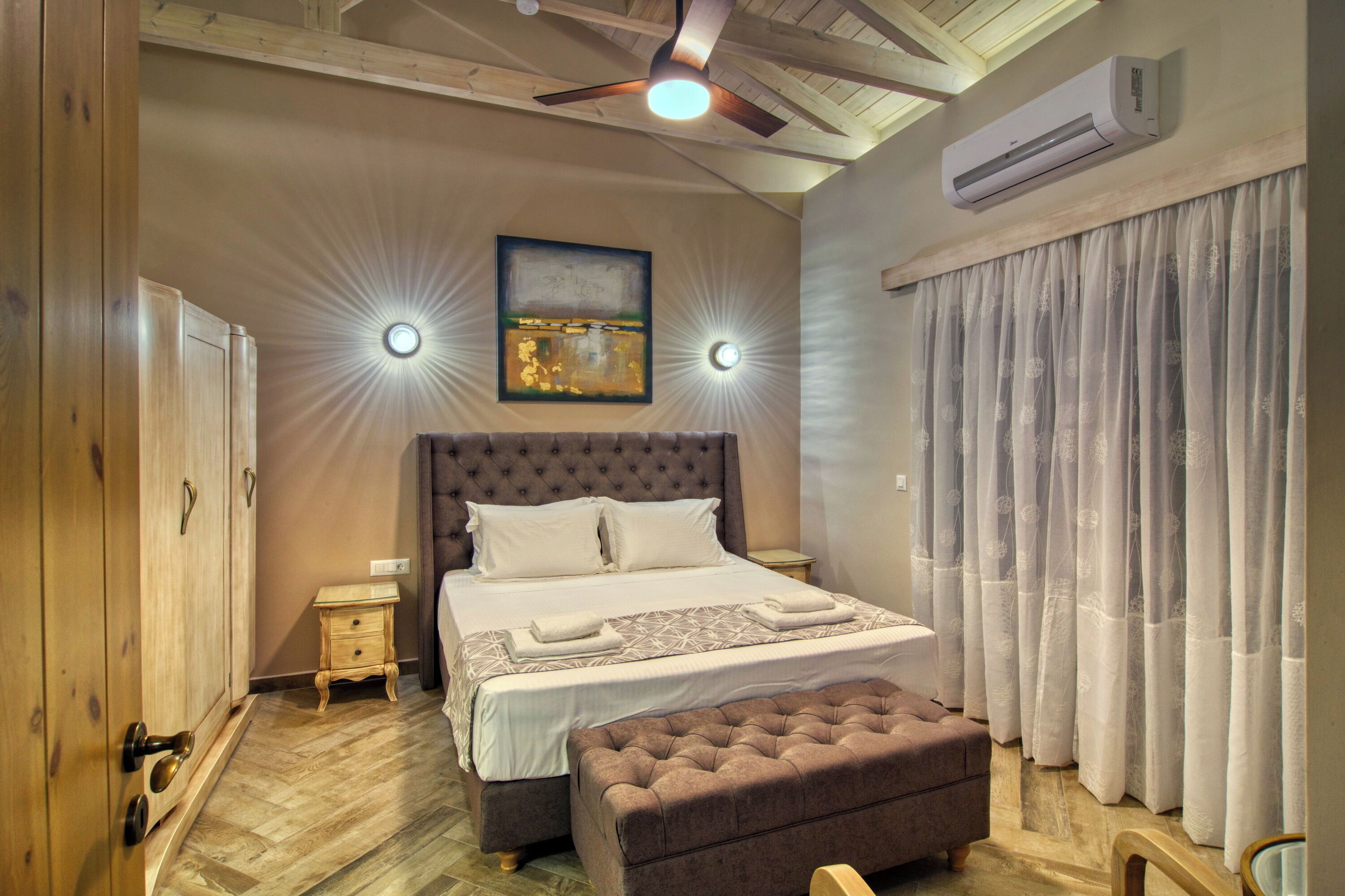 A bedroom with a large bed, a wooden wardrobe, a small bedside table, and a ceiling fan.