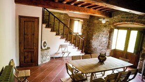 Un interior rústico con una escalera de madera, paredes de piedra, una mesa de comedor con sillas y un ventanal grande.