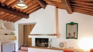 Una sala de estar acogedora con chimenea, sofá rojo, vigas de madera en el techo y un radiador blanco.