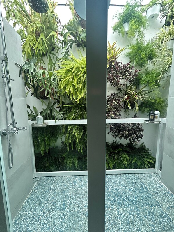 Une salle de bain équipée d’une douche, d’un lavabo et agrémentée de diverses plantes.