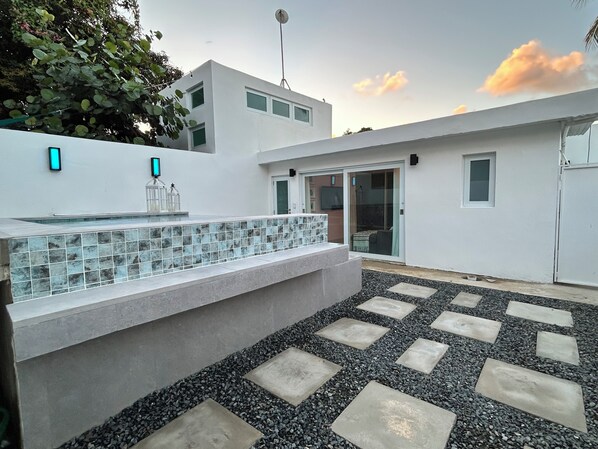 A modern outdoor area with a glass-tiled bench, a stone pathway, and a white building with a satellite dish.