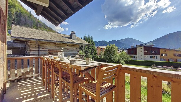 A wooden deck with a table and chairs, overlooking a mountain and a village.