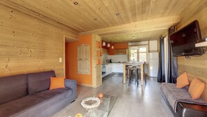 A cozy living room with a sofa and armchair, a glass coffee table, and a kitchen area with a dining table and chairs.