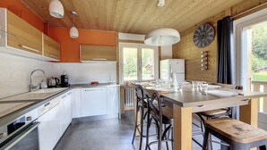 A modern kitchen with white cabinets, a central island with bar stools, and a large window providing a view of the outdoors.