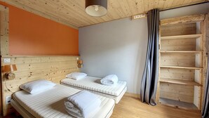 A room with two beds, wooden walls, a ceiling light, and a window with curtains.